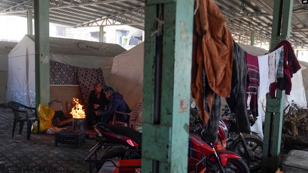 لاجئون سوريون يدفئون أنفسهم أمام خيام أقيمت في سوق عام كمأوى في مدينة إصلاحية في ولاية غازي عنتاب، جنوب تركيا، 11 شباط/فبراير 2023 (AP)