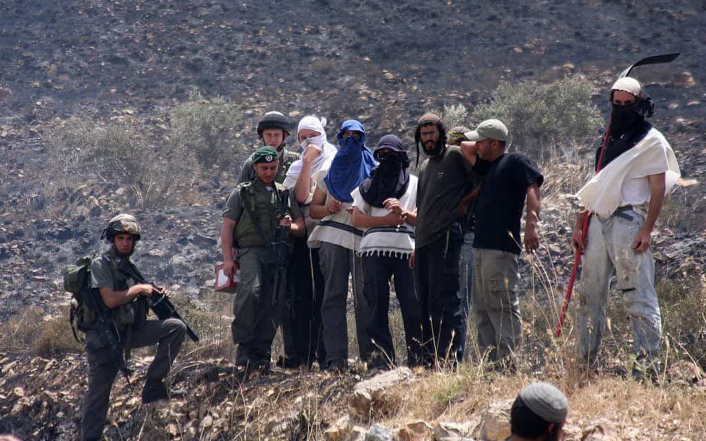 مستوطنون إسرائيليون ملثمون ويقف إلى جانبهم جنود من الجيش الإسرائيلي، الضفة الغربية المحتلة (الصحافة الإسرائيل - فلاش 90)