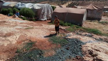 طفل يقف بالقرب من مياه الصرف الصحي في مخيم للمهجرين شمالي إدلب - رويترز