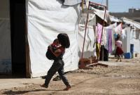 طفلة سورية لاجئة تحمل طفلاً بين يديها وهي تسير بين الخيم في أحد مخيمات سهل البقاع بلبنان