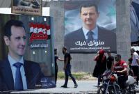 أشخاص يمرون بالقرب من ملصقات دعائية لرئيس النظام السوري بشار الأسد في دمشق - 22 أيار 2021 (رويترز)