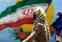 نساء يمشين بجانب رسمة جدارية للعلم الإيراني في أحد شوارع طهران - 17 حزيران 2021 (AFP)