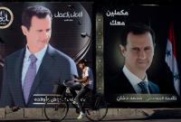 شاب يمر أمام ملصقات دعائية لرئيس النظام السوري بشار الأسد - 26 أيار 2021 (AP)