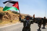 مواطن فلسطيني يحمل علم فلسطين وخلفه جنود إسرائيليين (رويترز)