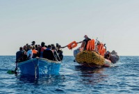 قارب يقل مهاجرين في البحر وبقربه قارب إنقاذ يوزع ستر نجاة