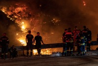 رجال الإطفاء ينظرون إلى حريق غابات مشتعل في جبل بارنيثا، في اليونان (رويترز)