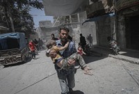 مدني يسعف طفلاً إثر غارة للنظام على ريف إدلب (الأناضول)
