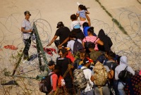 مهاجرون يعبرون سياجاً من الأسلاك الشائكة قرب الجدار الحدودي الذي يفصل الولايات المتحدة عن المكسيك - رويترز