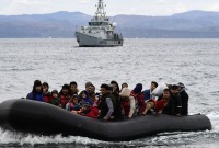 لاجئون في بحر إيجة وخلفهم سفينة تتبع لوكالة "فرونتكس" (AFP)