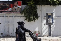 Women walks past a poster of Bashar al-Assad during Syria's first local elections since 2011, on September 16, 2018 in the southern Eastern Ghouta, on the eastern outskirts of the capital Damascus