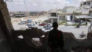 عنصر من قوات النظام يراقب المارّة من داخل بناء مهدّم في درعا البلد (أرشيفية/AFP)