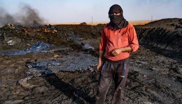 عامل سوري في مصفاة نفط مؤقتة وهو يقف فوق نفايات نفطية
