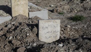 منظر يظهر شاهد قبر كتب عليه بالعربية "فتاة صغيرة مجهولة الهوية ترتدي سترة خضراء" داخل مقبرة في بلدة جندرس