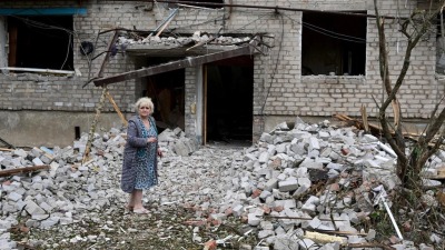امرأة تقف أمام المبنى المدمر بسبب الغارة الروسية اليوم الأحد 10 تموز 2022، شرق أوكرانيا (AFP)