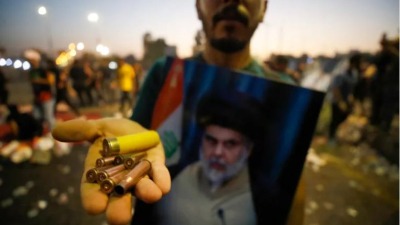 متظاهر عراقي يحمل صورة لمقتدى الصدر ورصاصات خلال مظاهرات في وسط العاصمة العراقية (إنترنت)