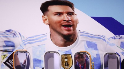  أحد أعضاء وفد المنتخب الأرجنتيني ينظر من نافذة الطائرة مع صورة ليونيل ميسي عليها 2022-الدوحة قطر (رويترز)