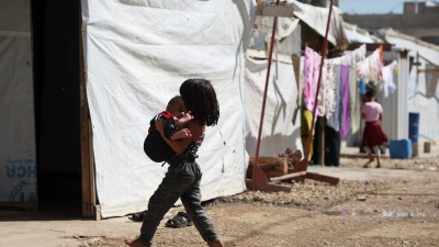 طفلة سورية لاجئة تحمل طفلاً بين يديها وهي تسير بين الخيم في أحد مخيمات سهل البقاع بلبنان