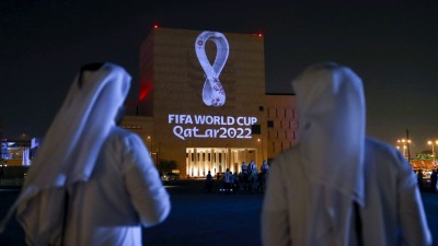 قطريون يقفون قرب سوق واقف بالعاصمة الدوحة حيث يُعرض الشعار الرسمي لمونديال "قطر ٢٠٢٢" - Getty