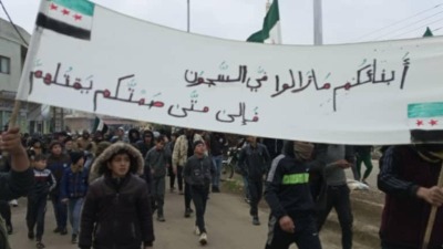 متظاهرون في مدينة جاسم شمالي درعا يحملون لافتة تطالب بالمعتقلين (تويتر)