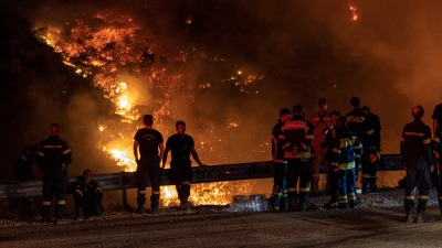 رجال الإطفاء ينظرون إلى حريق غابات مشتعل في جبل بارنيثا، في اليونان (رويترز)