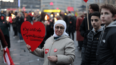سيدة سورية في الدنمارك تحمل لوحة كُتب عليها باللغة الإنجليزية: سوريا ليست آمنة - GETTY
