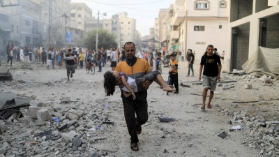 رجل فلسطيني يحمل طفلة جريحة من جراء قصف إسرائيلي على خان يونس جنوبي قطاع غزة - 14 تشرين الأول 2023 (رويترز)
