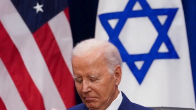 الرئيس الأميركي جو بايدن وخلفه علم بلاده وعلم إسرائيل