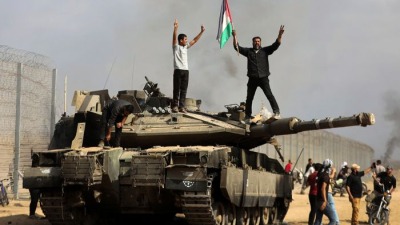 فلسطينيون يرفعون العلم الفلسطيني فوق دبابة إسرائيلية بالقرب من السياج الحدودي مقابل خانيونس، 7 تشرين الأول/اكتوبر 2023 (متداول)
