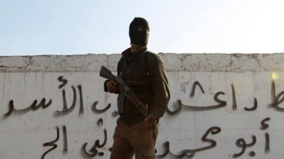 مقاتل من الجيش السوري الحر يقف أمام كتابات مكتوب عليها "داعش يسقط" في حلب