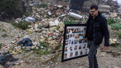 شخص يحمل لوحة في صور بعض ضحايا الزلزال في هاتاي (رويترز)