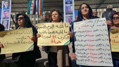متظاهرون في ساحة الكرامة وسط السويداء يحملون لافتات تندد بمجزرة حماة - 21 شباط 2024 (السويداء 24)