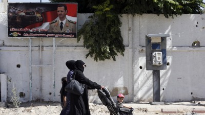 Women walks past a poster of Bashar al-Assad during Syria's first local elections since 2011, on September 16, 2018 in the southern Eastern Ghouta, on the eastern outskirts of the capital Damascus